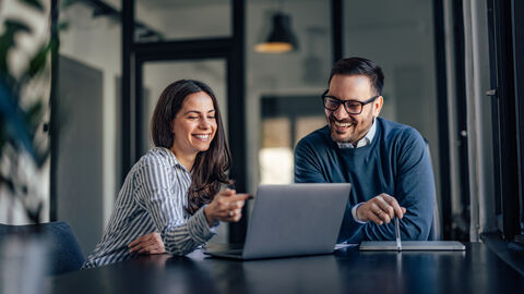 Frau und Mann in Gesprächssituation vor einem Laptop sitzend