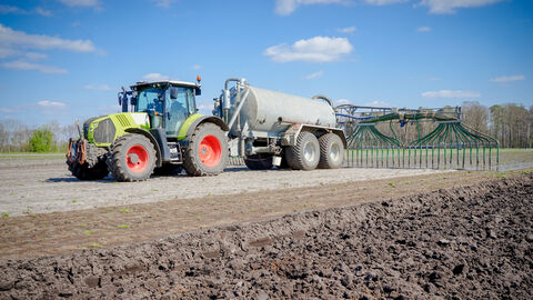 Klärschlammverordnung Traktor in Aktion bei Gülleausbringung mit Güllefass und Schleppschlauchgestänge