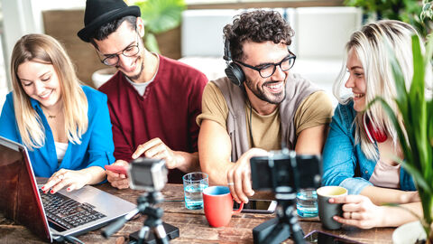 Vier Personen, die mit Smartphones, Kameras und Laptops Social Media Inhalte bearbeiten.