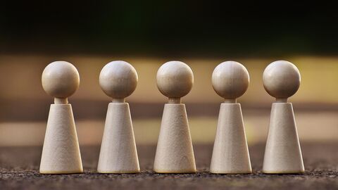 5 Spielfiguren aus Holz stehen versammelt nebeneinander.