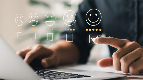 Eine Person die am Laptop sitzt und auf ein Lachsmilie drückt. 