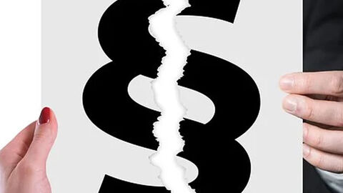 Eine Frauen- und einen Männerhand halten einen Zettel mit einem Paragraphenzeichen, der gerissen ist.