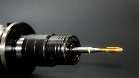 Maschinen Ein Gewindebohrer mit goldenem Aufsatz vor schwarzem Hintergrund.