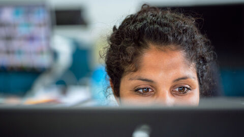 VBL / Zusatzversorgung Eine dunkelhäutige Frau schaut auf einen Bildschirm / Monitor. Man sieht nur die Augen und im Hintergrund eine unscharfe Büroperspektive.