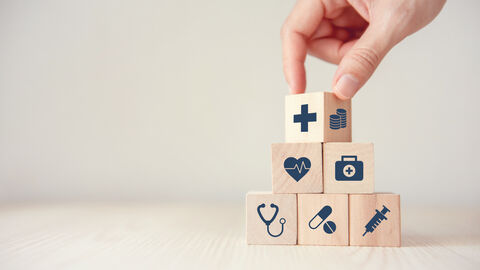 Eine Hand, die kleine Würfel mit medizinischen Icons aufeinander setzt.