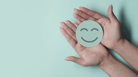 Zwei Hände halten einen Button mit einem lachenden Smilie.