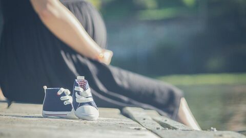 Schwangere Frau sitzend und kleine Babyschuhe davon.