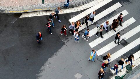 Mehrere Menschen gehen in einer Stadt über einen Zebrastreifen.