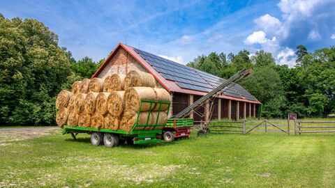 Heuwagen mit Heuballen von einer Scheune von Photovoltaikplatten.