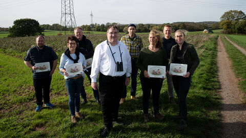 Regierungspräsident Mark Weinmeister und Projektbeteiligte auf einer Wiese, nahe dem Rebhuhn-Projekt.