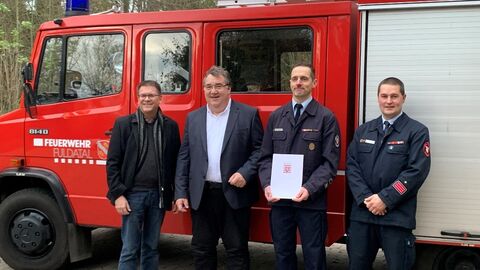 Regierungspräsident Mark Weinmeister übergibt, vor einem Feuerwehrauto, einen Bescheid an den Bürgermister von Fuldatal. 