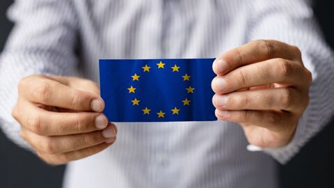 Kleine Europa-Fahne die von zwei Händen in Richtung Kamera gehalten wird.