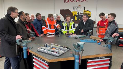 RP Weinmeister steht bei einer Firmenbesichtigung mit mehreren Personen um einen Tisch.