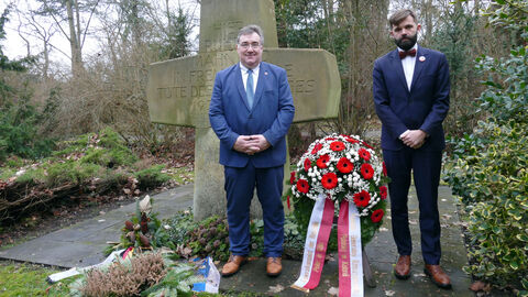 Regierungspräsident Mark Weinmeister und Generalkonsul Jakub Wawrzyniak vor einem großen Stein und der Kranzspende
