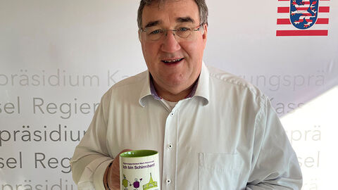 RP Mark Weinmeister mit einer Tasse in der Hand. Aufschrift: Schirmherr Kleine Riesen.