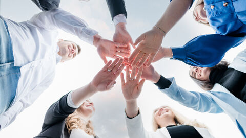 Menschen, die ihre Arme und Hände aneinanderhalten, sodass eine Art Stern entsteht.