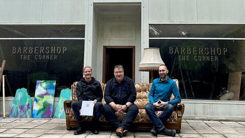 Drei Personen auf einer Bank, die vor einem Gebäude steht