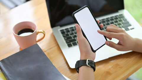 Eine Person am Schreibtisch mit Tablet-PC, Handy und Kaffeetasse