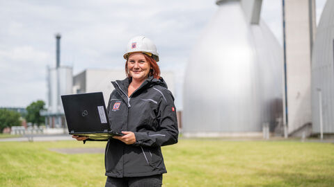 Person mit Laptop in der Hand vor Faultürmen
