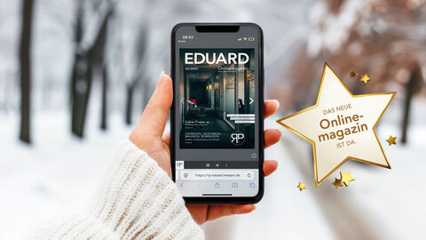 Winterlandschaft im Hintergrund. Frauenarm im weißen Pullover mit Handy in der Hand im Vordergrund. Zu sehen ist die Titelseite des neuen EDUARD.