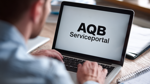 Mann sitzt vor einem Laptop auf dem man AQB-Serviceportal lesen kann.