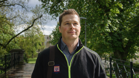 Ein Mann in Arbeitsjacke geht auf einem von Bäumen umgebenen Weg im Freien